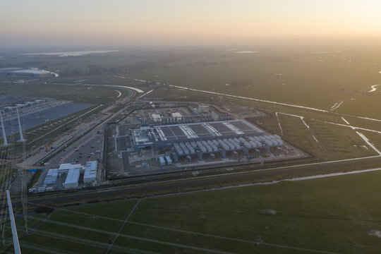 Aerial view of the Google data center facility with cooling systems and power infrastructure surrounded by green fields during sunset.