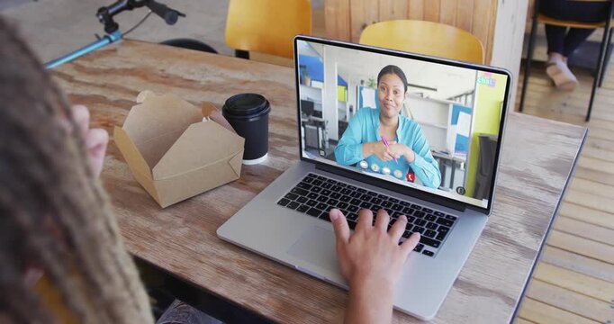 Vertical video: Man answering business call on laptop in coffee shop, typing and snacking