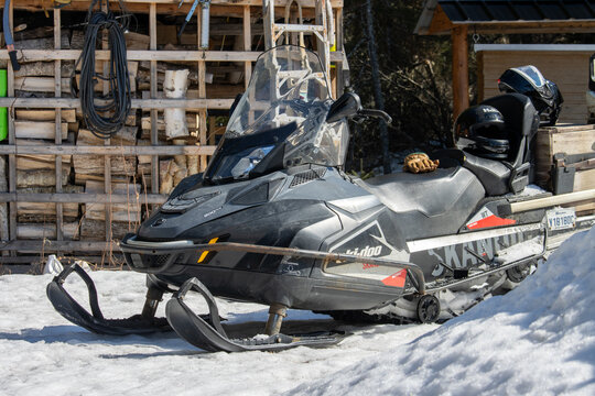 Canada, 11 April 2026 : Ski-Doo snowmobile with Rotax engine and HJC helmets parked in snow near woodpile