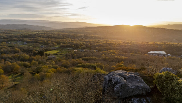 Aerial view of the rolling hills and dense forests of Allariz under a golden sunset sky with rocky outcrops in the foreground Allariz, Province of Ourense, Spain.