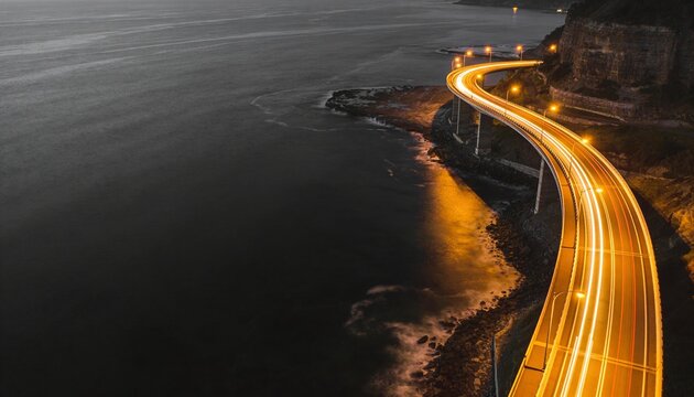 Glowing viaduct hugging cliff, casting amber vehicle light trails with lamps over ocean, copy space