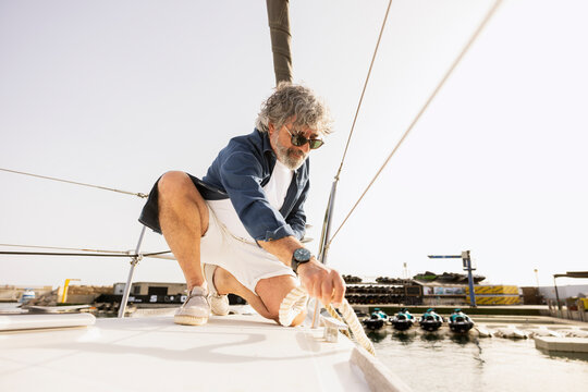Mature man pulling rope on a yacht deck, enjoying a luxury sailing lifestyle