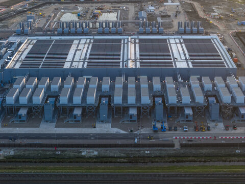 Aerial view of a large data center AI facility with rows of cooling units and industrial infrastructure under a soft evening light Netherlands.