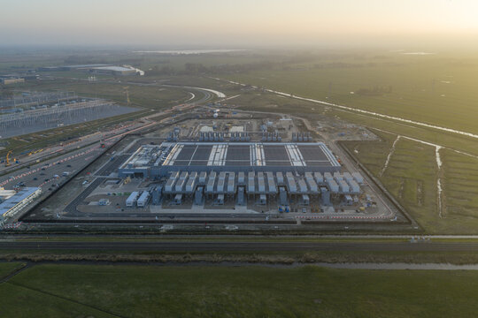 Aerial view of a large modern data center facility with cooling units and industrial infrastructure surrounded by green fields at sunset Netherlands.