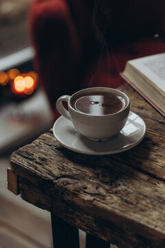 Home decor and comfort. A book, glasses, and a cup of tea on a wooden table. A sitting area in a cozy room. 