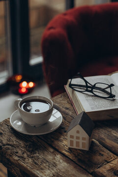 Home decor and comfort. A book, glasses, and a cup of tea on a wooden table. A sitting area in a cozy room. 