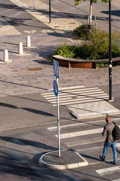 Man pedestrian crossing at crosswalk on urban street during commute as traffic passes in sunlight and shadows mark every step across the lane