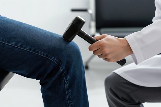 Doctor checks patient knee reflex with hammer in clinic. Physician performs medical test. Person in white coat examines leg for nerve response. Health checkup in hospital office.