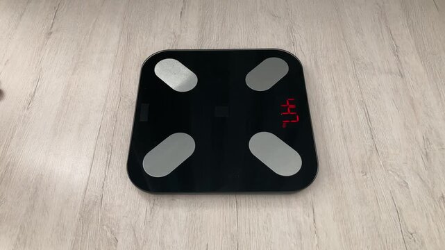 A woman stands on a floor scale and waits for the result. Weight loss. The importance of small steps on the way to weight loss. Attention to your own health and body