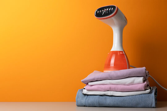Stylish Portable Steaming Appliance Displayed Alongside Organized Textiles Against Bright Orange Background