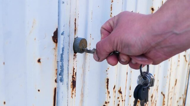 Close-up of worker hand closing lock with key on old rusty door in workshop. Ideal for safety concepts, industrial visuals, access control themes