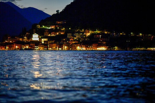 Das beleuchtete Fischerdorf Peschiera Maraglio mit der Pfarrkirche San Michele Arcangelo am Ufer der Monte Isola bei Abendd&auml;mmerung, Iseosee