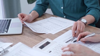 Fototapeta premium Auditor man wearing green shirt is reviewing papers and using a laptop with the colleague. Business people professionals analyzing financial documents. Finance, audit, and taxes