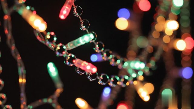 Vibrant multicolored festive lights ascending through a beaded holiday garland against a dark shadowy background creating a magical glowing Christmas atmosphere for seasonal celebration.