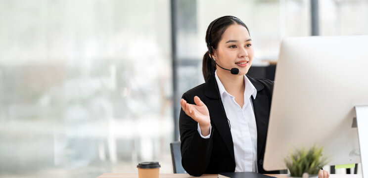 Asian Customer Support Agent with Headset Focusing on Computer Screen in Office