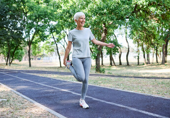 Fototapeta premium Portrait of a senior mature woman exercising, stretching, warming up, running and jogging outdoors in the park
