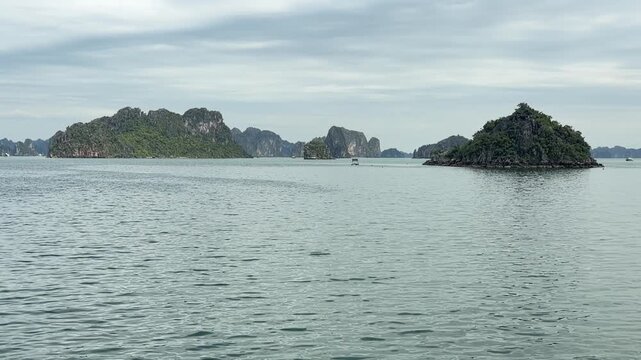 Scenic limestone islands rising from calm waters in Halong Bay Vietnam, tranquil marine landscape, travel destination, natural wonder, seascape