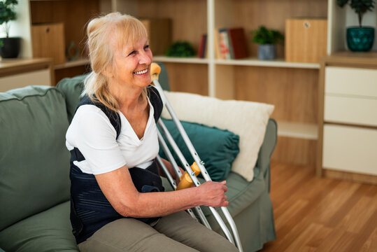 Happy senior woman wearing back support brace is sitting on bed at home. She is happy after successful recovery from injury.