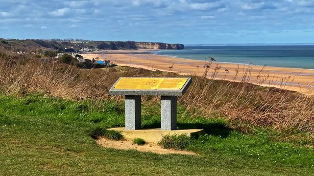 A historical sign stands above Omaha Beach, offering sweeping views of the coastline and cliffs.