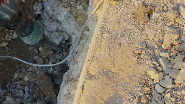 Top view of drilling machine working in dug trench with soil and rocks scattered around, rough terrain and equipment visible in an outdoor construction setting