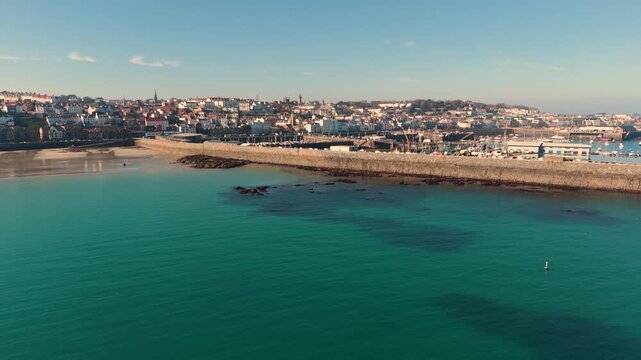 Havelet Bay St Peter Port Guernsey.Panning footage of the bay from the beach to Castle Cornet with clear blue water and the harbour as its backdrop in late afternoon sun with cloudless sky