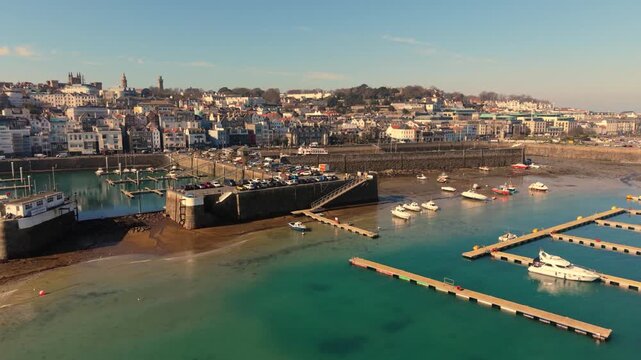St Peter Port Harbour Guernsey.Slow forward golden hour flight to Victoria Marina at low tide showing inside the visitor&rsquo;s marina,Crown Pier with town backdrop and clear blue sky