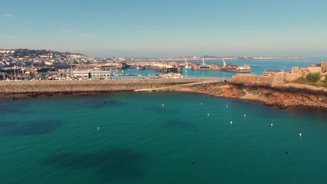 Havelet Bay St Peter Port Guernsey.Panning footage of the bay and seawall to Castle Cornet with clear blue water and the harbour as its backdrop in late afternoon sun with cloudless sky