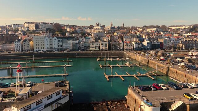 St Peter Port Harbour Guernsey.Slow forward golden hour flight over the cill through the entrance to Victoria Marina at low tide showing Crown Pier with town backdrop and clear blue sky