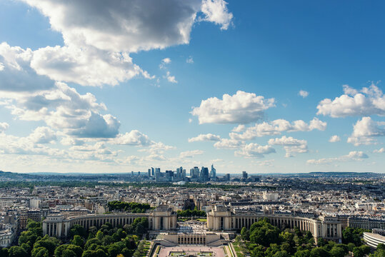 Aerial view of the Palais de Chaillot at Trocadero with the modern skyscrapers of La Defense on the horizon under a bright cloudy sky in Paris, Ile-de-France, France.