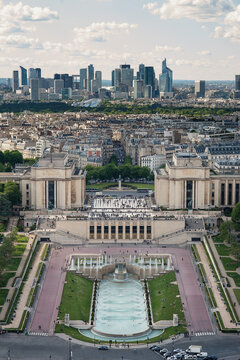 Aerial view of the Trocadero Gardens and Palais de Chaillot with people walking near the fountains and the modern La Defense skyline in the distance in Paris, Ile-de-France, France.