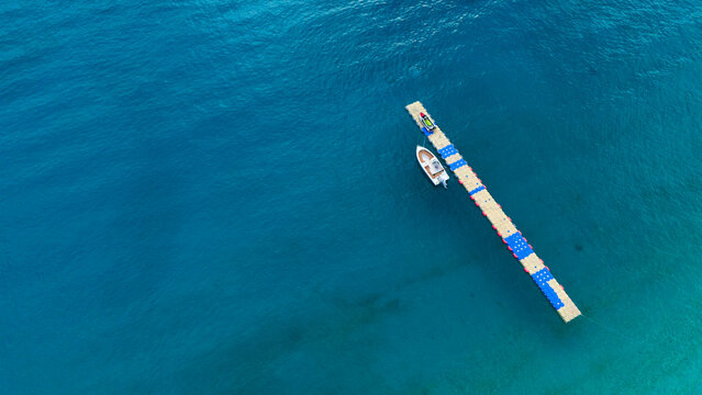 Spectacular high angle aerial perspective of a solitary small white boat anchored alongside a colorful modular plastic pontoon dock floating peacefully in crystal clear deep blue ocean