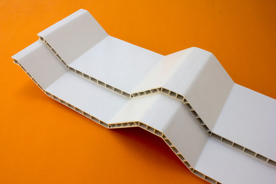 White UPVC roof pieces on orange background. UPVC (Unplasticized Polyvinyl Chloride) roofing sheets are durable, lightweight, and weather-resistant panels designed for residential and industrial use. 