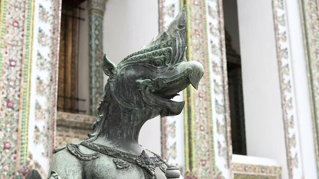 Ancient bronze garuda statue guarding white ornate temple at wat phra kaew in bangkok thailand.
