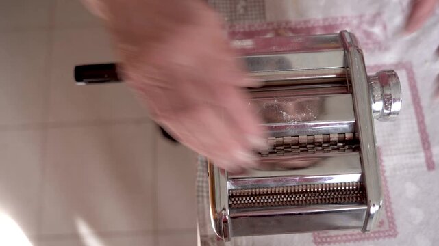 hand of old italian grandma making fresh handmade tagliatelle pasta with manual pasta machine, italian food with warm natural light, healthy nutrition
