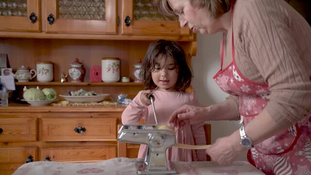 italian grandma with grandchild making fresh handmade tagliatelle pasta with hand pasta machine, grandma with children doing activity