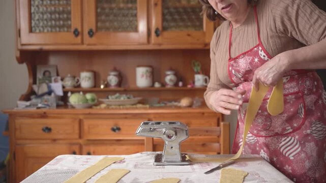 hand of old italian grandma making fresh handmade tagliatelle pasta with manual pasta machine, italian food with warm natural light, healthy nutrition