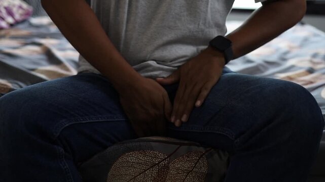 Asian man sitting on the bed, suffering from prostate and bladder problem. Close up