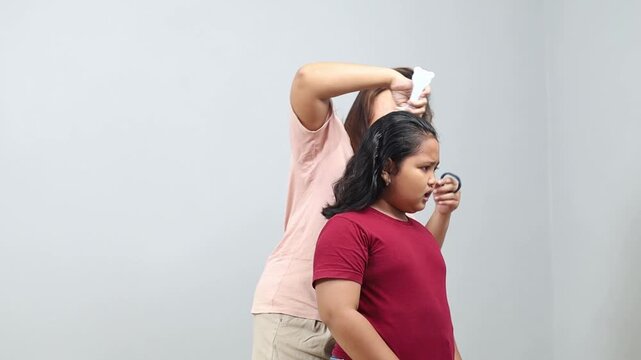 Mother is trying to tie a ponytail, but as she pulling hair, daughter is almost crying