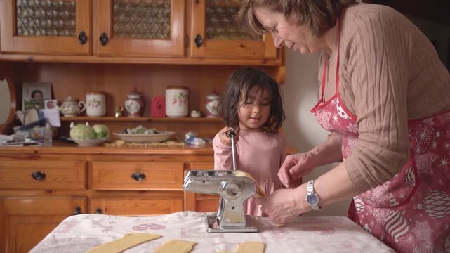 italian grandma with grandchild making fresh handmade tagliatelle pasta with hand pasta machine, grandma with children doing activity