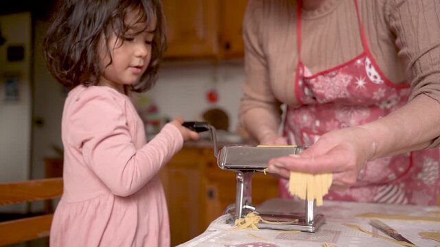 italian grandma with grandchild making fresh handmade tagliatelle pasta with hand pasta machine, grandma with children doing activity