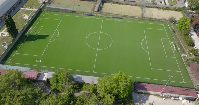 Aerial view of a well-maintained, lush green artificial turf soccer pitch featuring crisp white boundary lines, goals at both ends, and a central circle in a professional sport setting. It's empty.