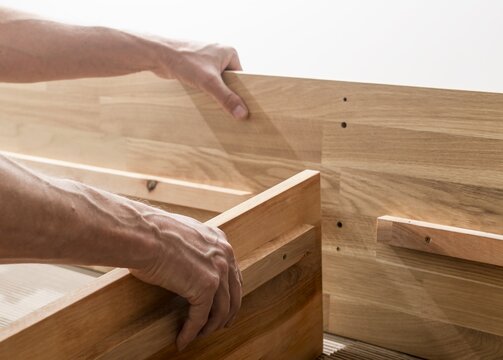 Hands assembling wooden furniture. Close up of carpentry work with boards and joinery. DIY home improvement and woodworking in a studio setting..