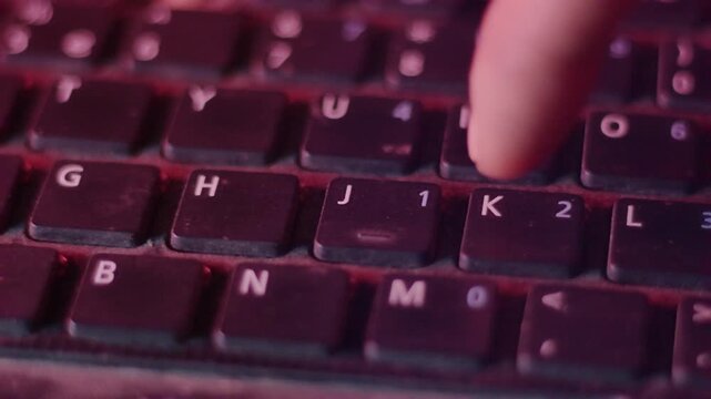 Person Finger Typing on Dusty Laptop Keyboard with Dramatic Red Lighting Macro Shot