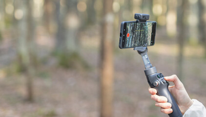 Smartphone on a handheld gimbal in a forest. Mobile video recording setup for outdoor content creation. Nature background with travel and vlogging technology.. © valiantsin