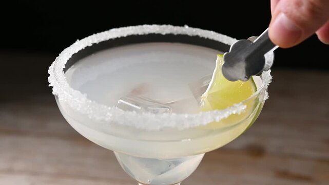 Bartender adding lime wedge to margarita cocktail. Close up