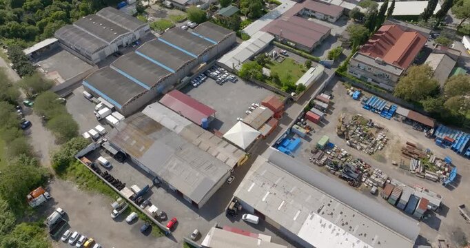 Aerial perspective of a dense industrial district with large warehouses, storage depots, and loading areas. The site features various trucks, parked cars, and diverse construction materials.