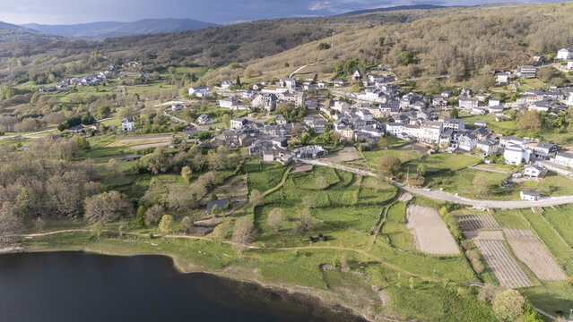 Aerial view of the village of A Veiga and the Encoro de Prada reservoir surrounded by green terraced fields and forested hills in A Veiga, Ourense, Spain.