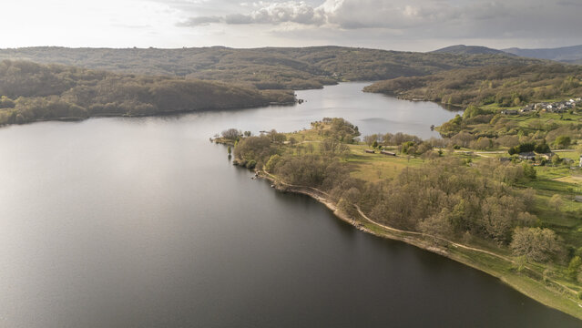 Aerial view of Encoro de Prada reservoir surrounded by lush forested hills and small villages under a soft sky A Veiga, Ourense, Spain.
