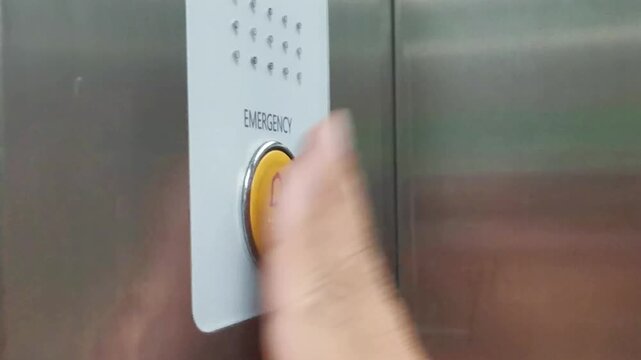 Hand pressing large yellow emergency button on metallic elevator panel