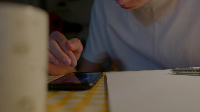 Focused study scene, Person studying deeply with writing tools and electronic device, Quiet home environment shows student preparing for exams with active notetaking and device usage